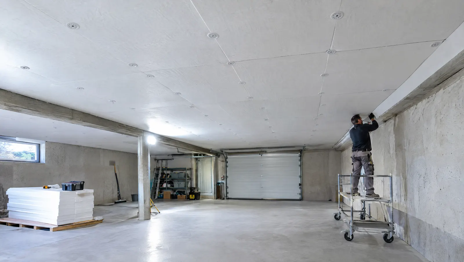 Plafond d’un sous-sol de maison isolé par des panneaux isolants blancs, artisan finissant la pose